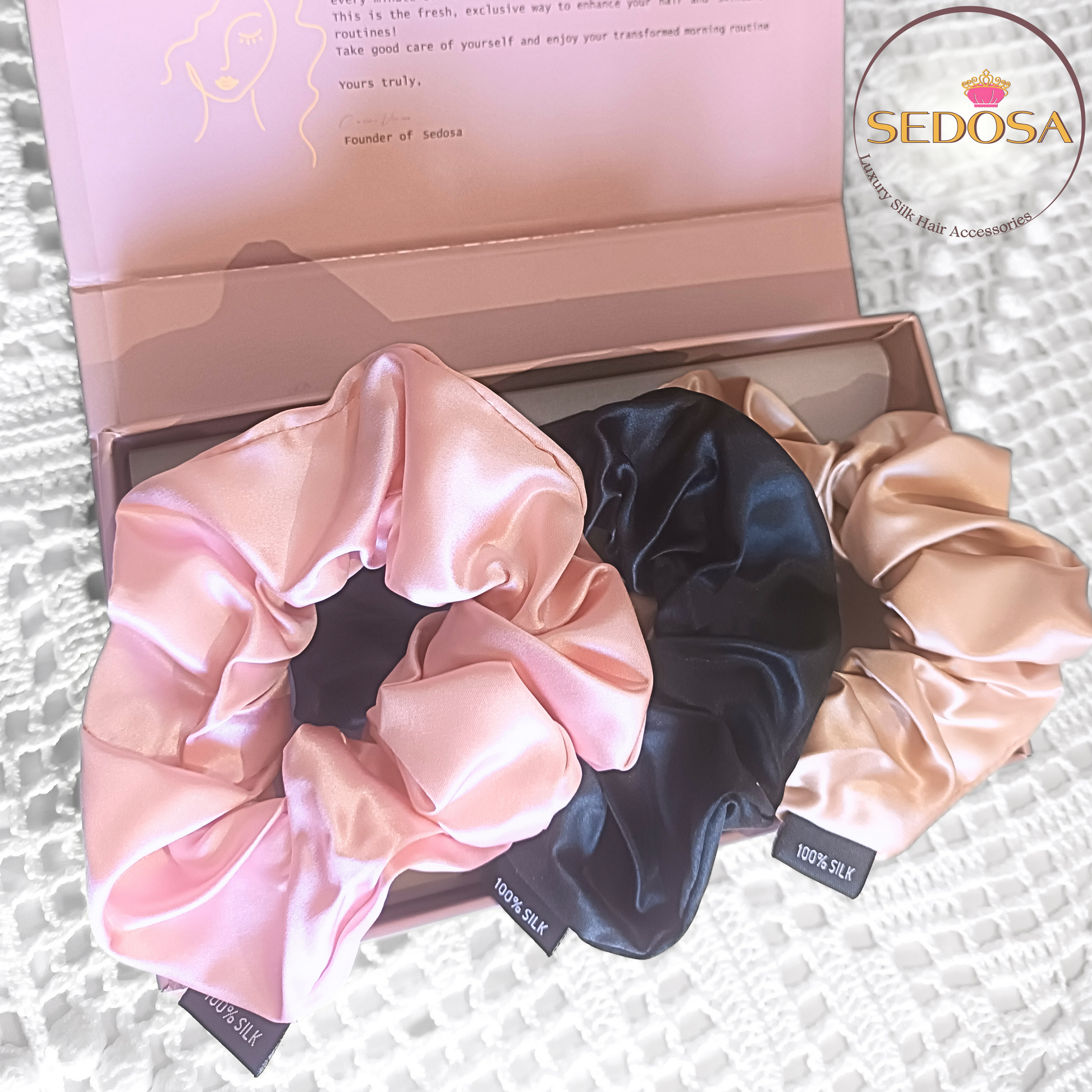 Set of silk hair scrunchies in pink, black, and caramel, large sized, with a SEDOSA branded box in the background.