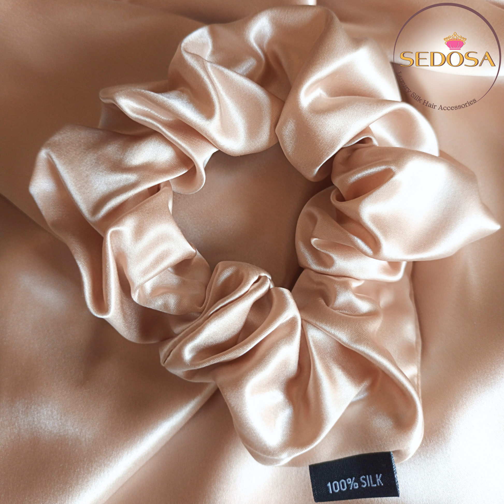 Caramel silk hair scrunchie sized large on a beige smooth silk fabric background with SEDOSA branding.