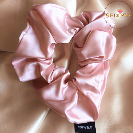 Pink silk hair scrunchie sized large on a beige smooth silk fabric background with SEDOSA branding.