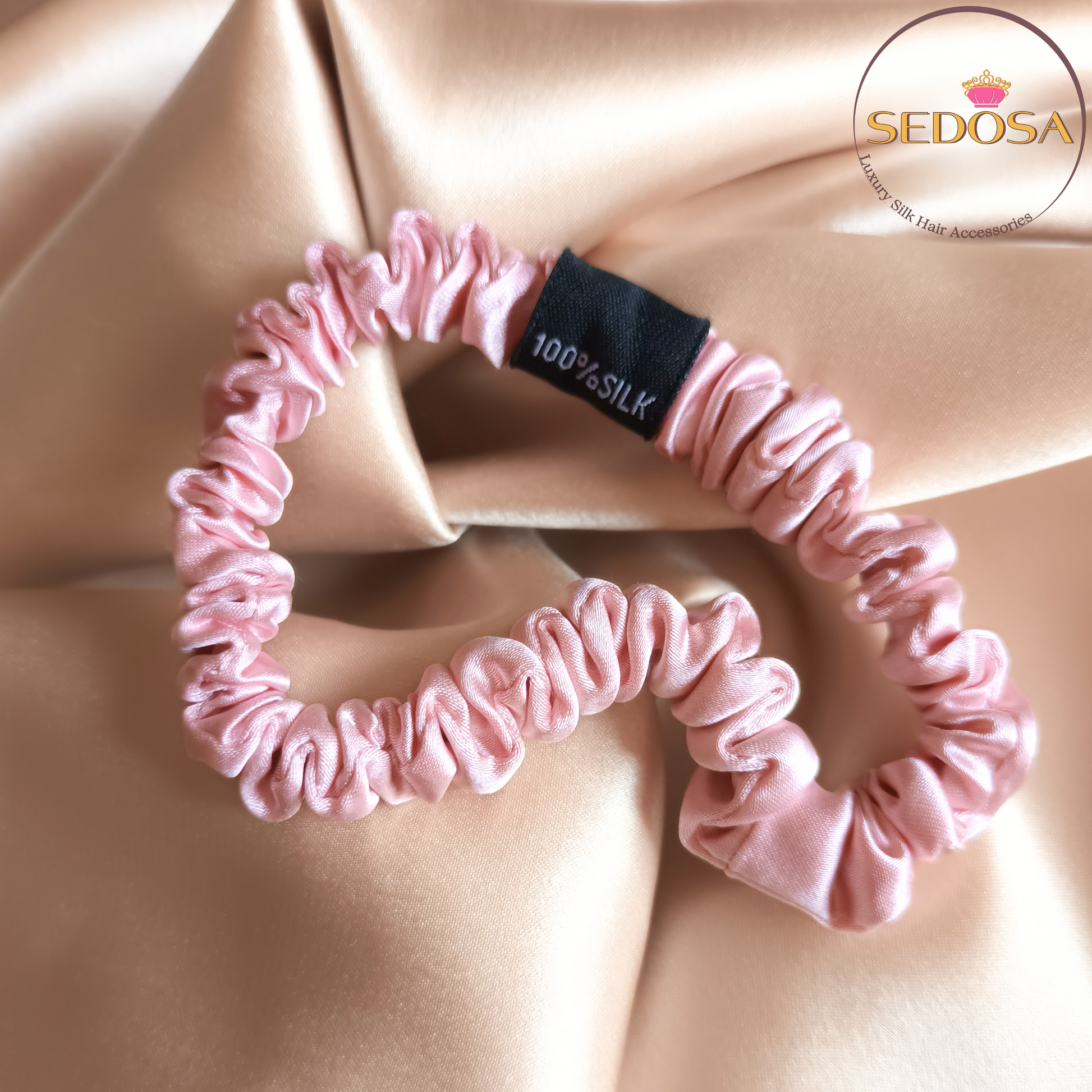 Pink silk hair scrunchy sized skinny on a silk smooth surface with SEDOSA branding